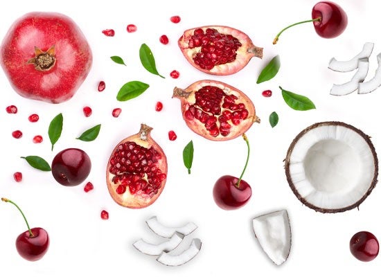 Pomegranate halves, cherries, coconut pieces, and green leaves scattered on a white background