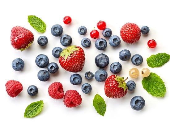 Assorted berries and mint leaves scattered on a white background